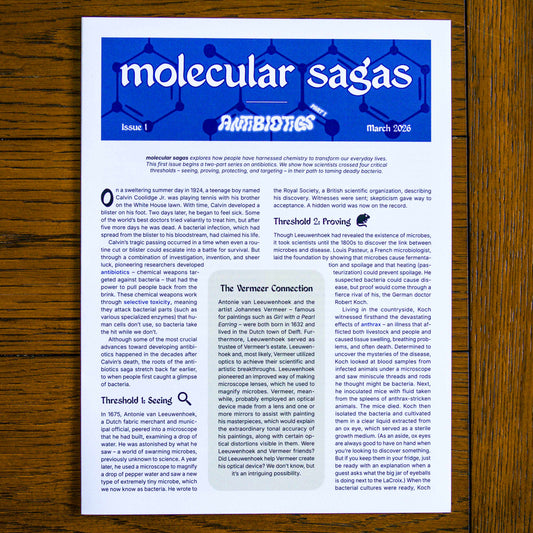 Paper publication titled 'molecular sagas' on a wooden background. Headings on the publication read 'Issue 1', 'Antibiotics Part 1', and 'March 2026'.