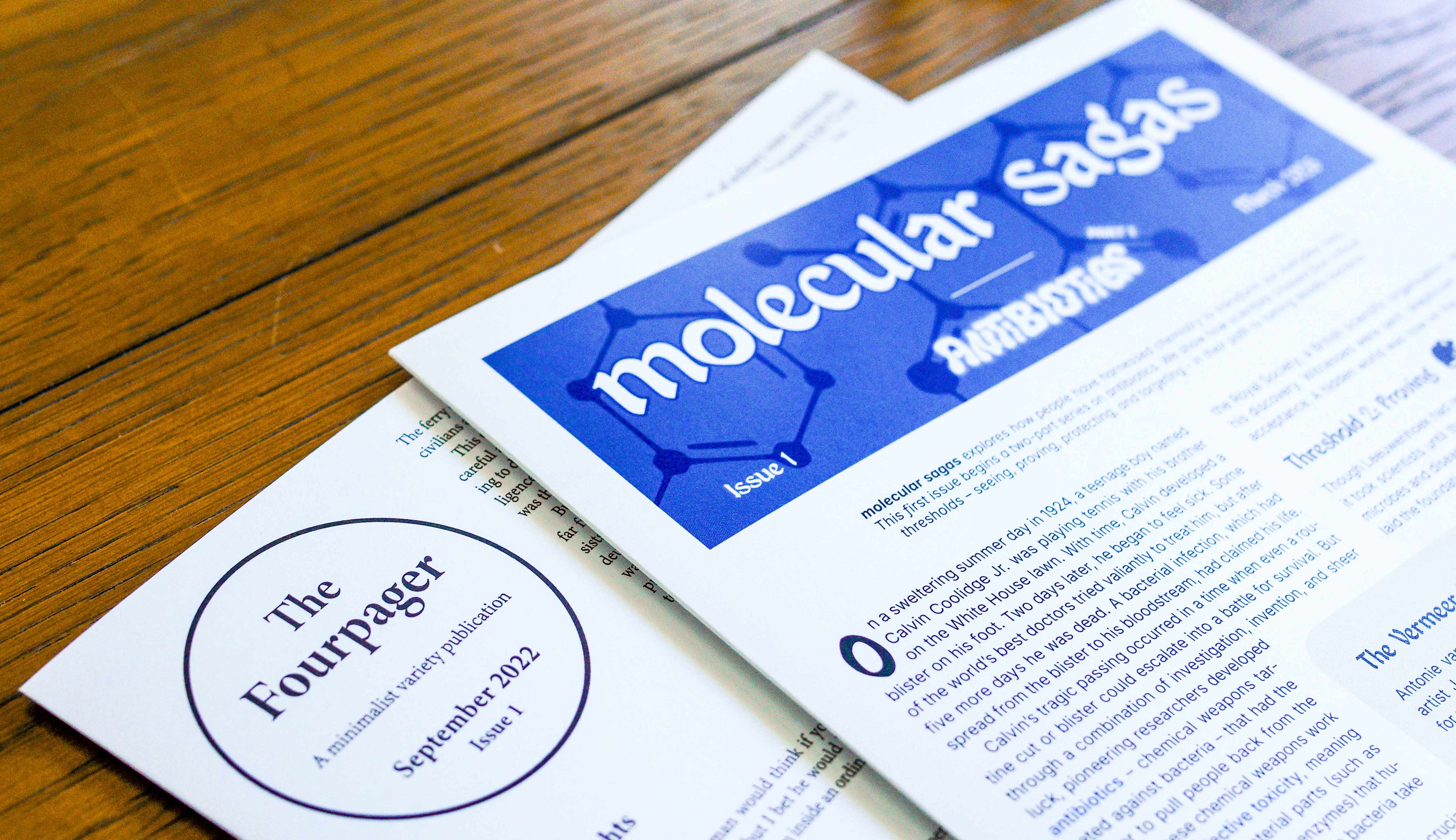 Stack of two publications, one titled 'The Fourpager', the other titled 'molecular sagas', on a wooden background